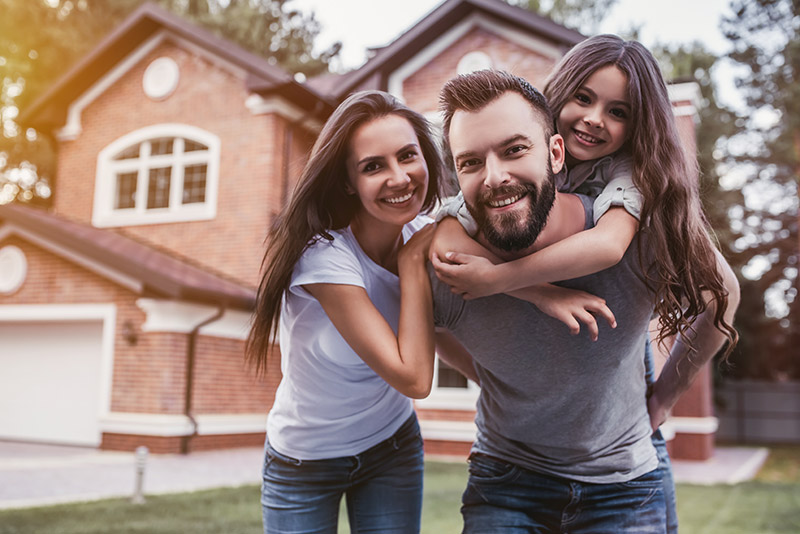 Family of 3 smiling in front of house